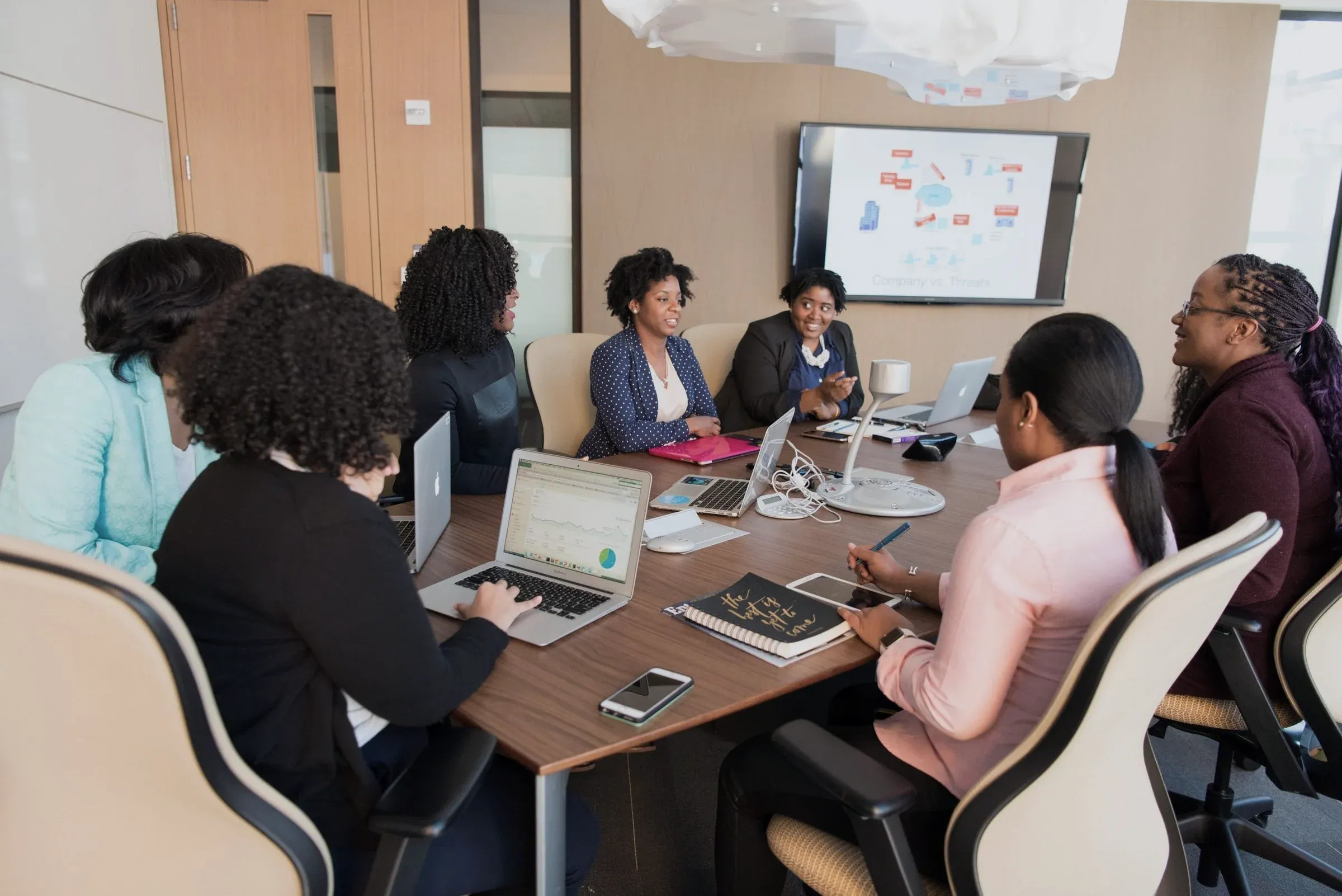 Colleagues meeting around a boardroom table with a presentation screen behind them